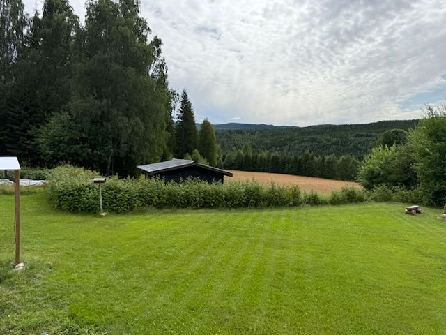Mown grass and forested hills in northern Värmland, with a small dark outbuilding
